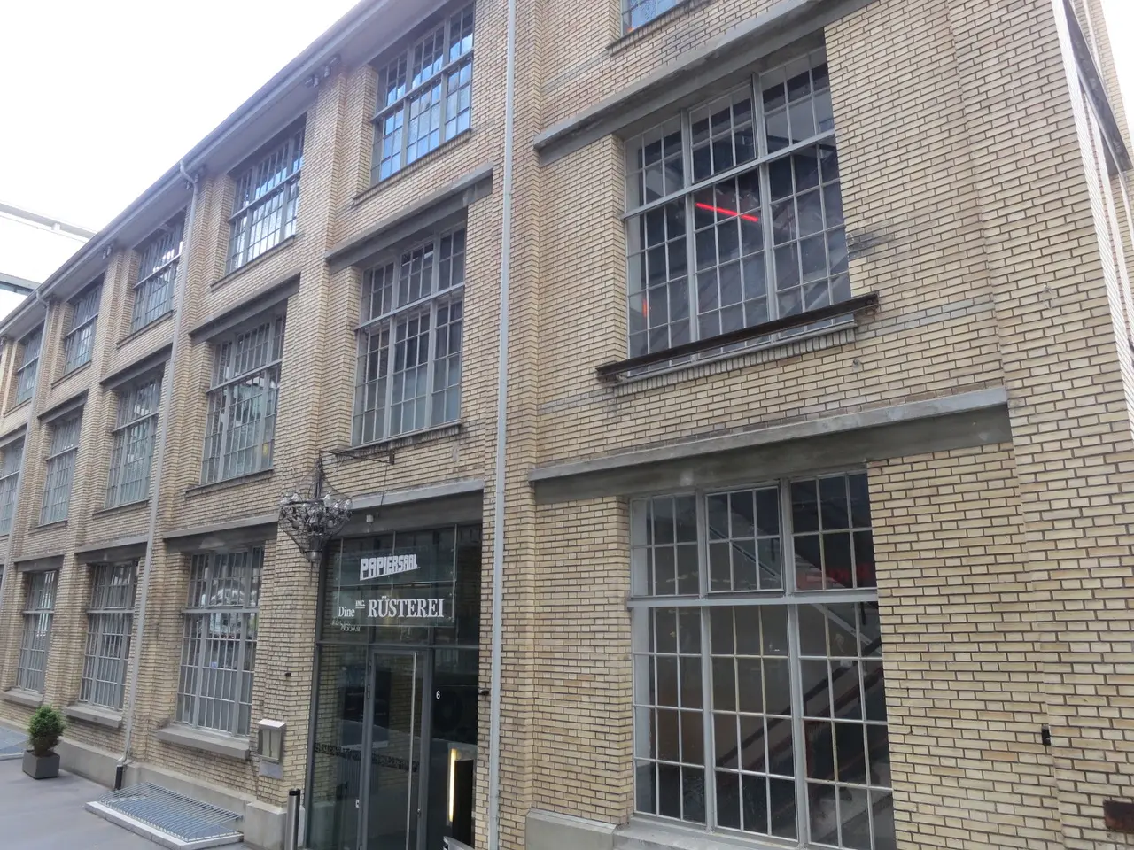 Facciata in mattoni dell'ex edificio industriale dell'area Sihlcity con grandi finestre a riquadri, sopra l'ingresso le insegne Papiersaal e Rüsterei