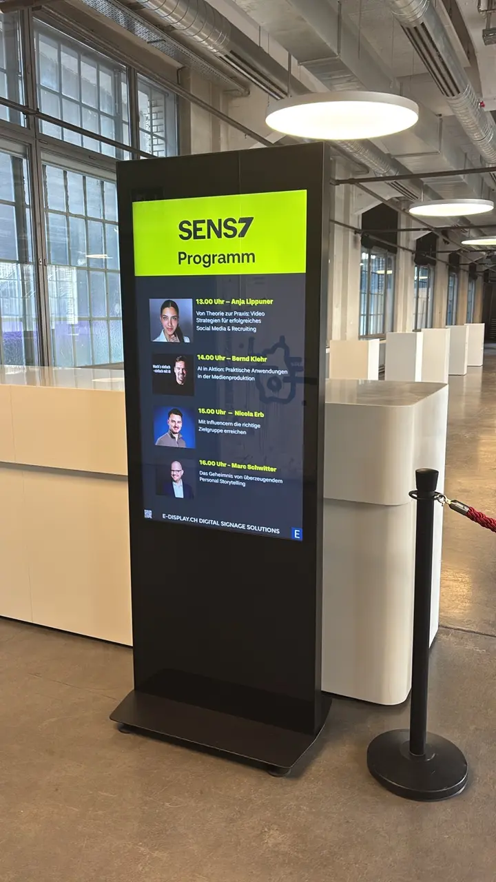 Totem digitale del programma con il logo SENS7 e i relatori nell'ingresso del Papiersaal